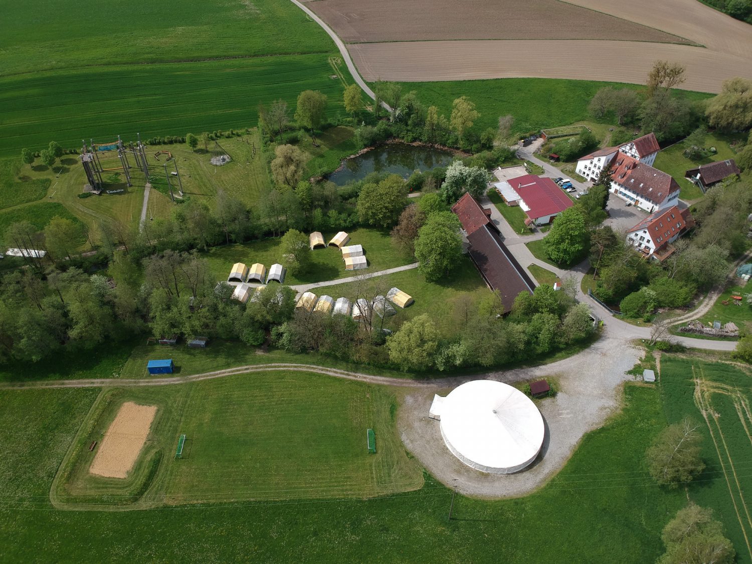 Luftbild über das gesamte Gelände der Dobelmühle mit Hochseilgarten, Badesee, Zeltinsel, Gebäuden und Zirkuszelt.